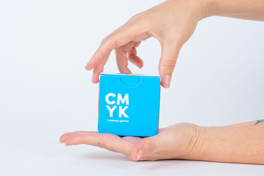 Hand holding a small blue cube with 'CMYK' text on a light gray background