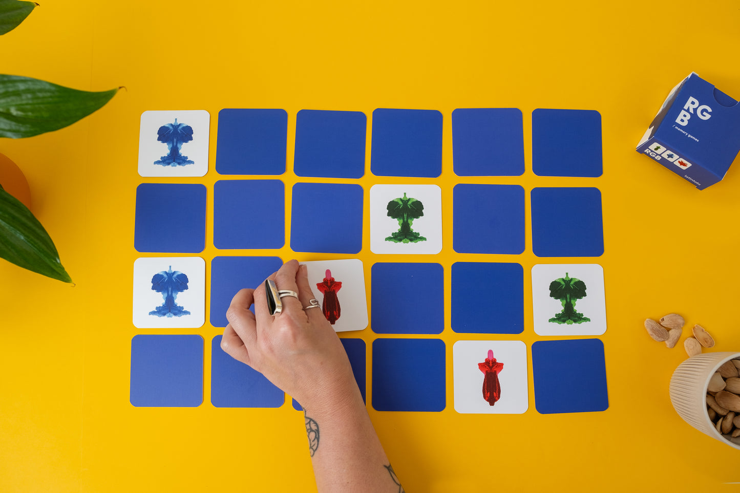 RGB Abstract memory game being played. Hand placing a card with a red figure on a grid of blue and white cards on a yellow surface.