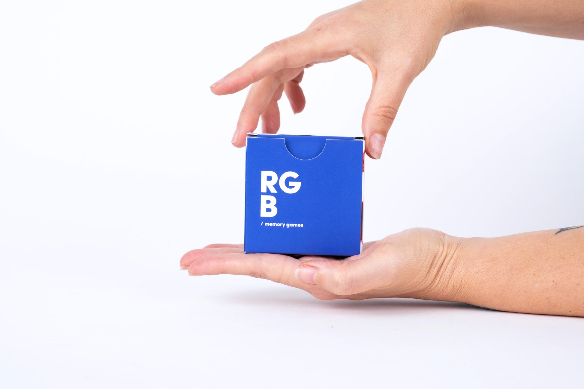 Blue cube with 'RGB' and 'memory game' text held in a hand against a white background